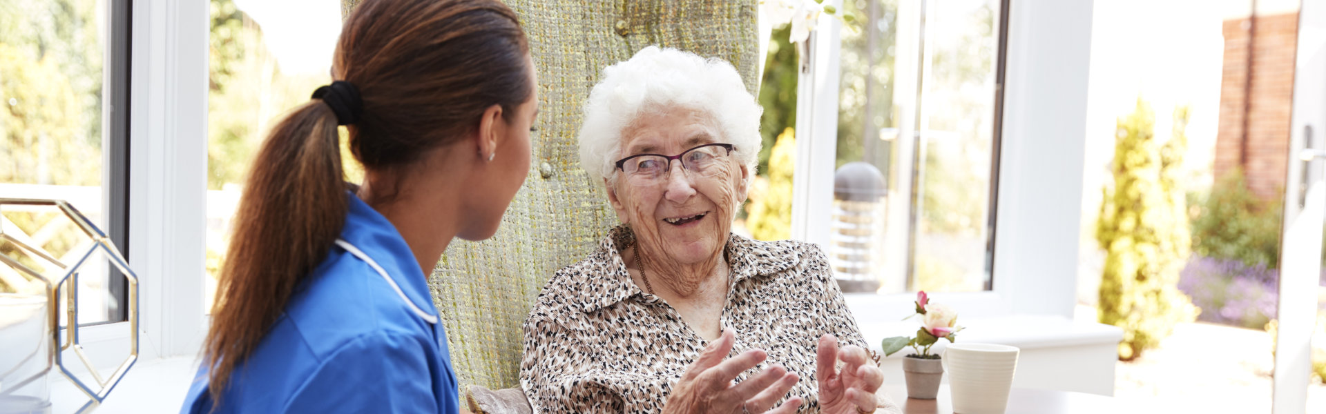 Woman Sitting In Chair And Talking With Nurse In Retirement Home